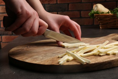 Photo of Woman cutting delicious fresh ripe parsnip at black table, closeup