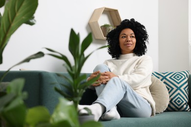 Relaxing atmosphere. Woman sitting on sofa near beautiful houseplants at home