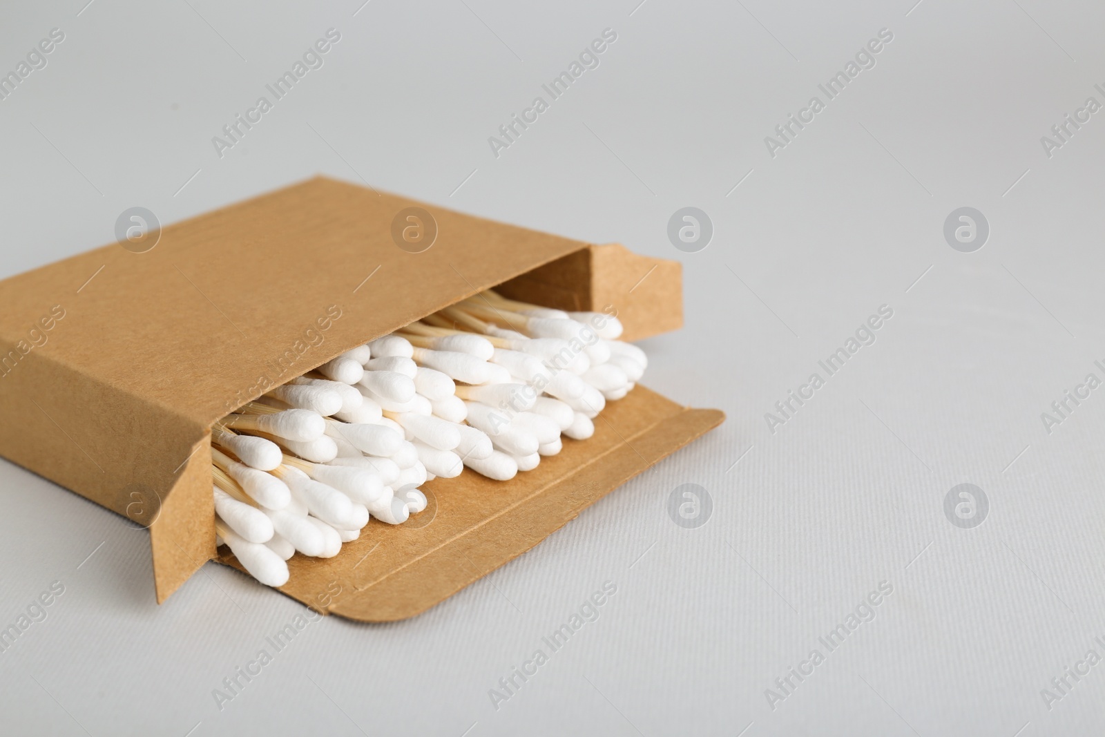 Photo of Box with wooden cotton buds on light grey background. Space for text