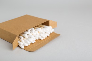 Box with wooden cotton buds on light grey background. Space for text