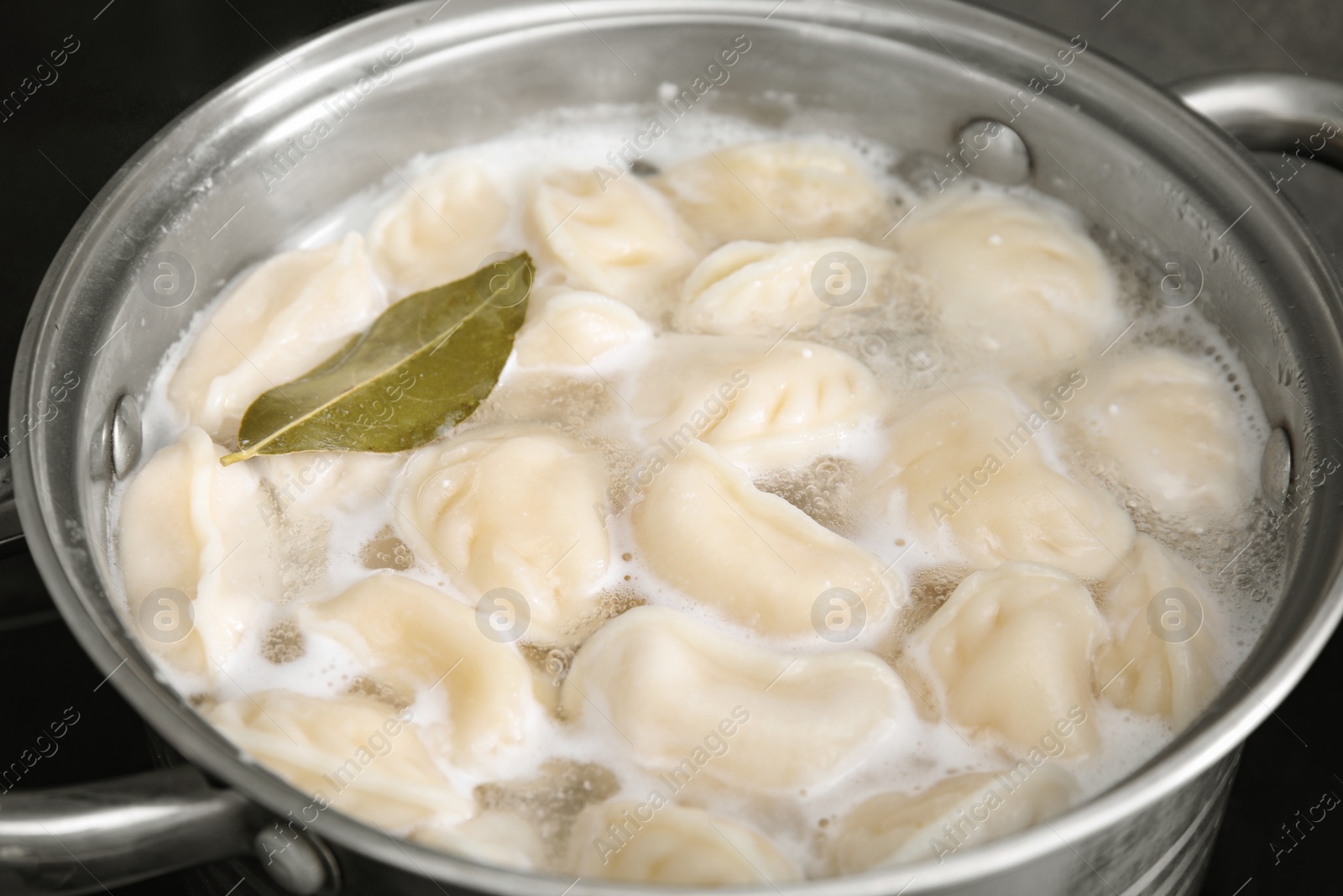 Photo of Cooking dumplings (varenyky) with tasty filling and bay leaf in pot, closeup