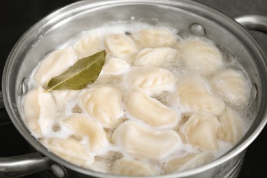 Cooking dumplings (varenyky) with tasty filling and bay leaf in pot, closeup