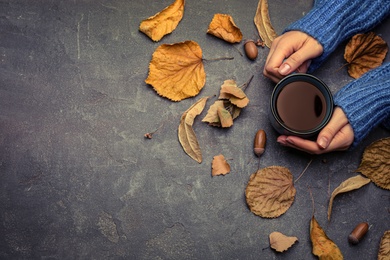 Woman with cup of hot drink at grey table, top view with space for text. Cozy autumn atmosphere