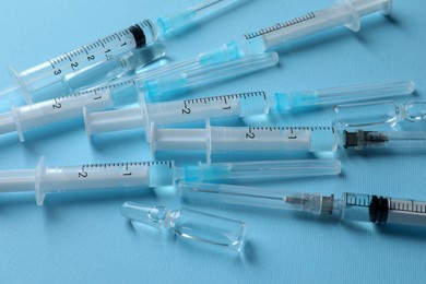 Photo of Disposable syringes with needles and ampules on light blue background, above view