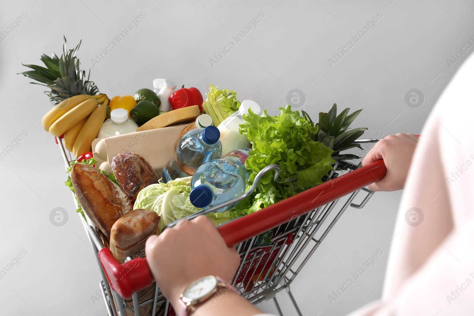 Photo of Woman with shopping cart full of groceries on grey background, closeup