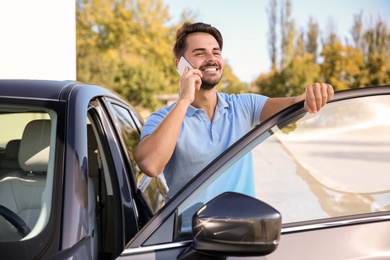 Young man talking on phone near modern car, outdoors