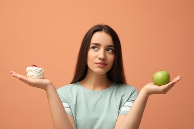 Photo of Woman choosing between apple and cake on orange background