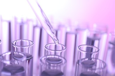 Dripping liquid from pipette into test tube on violet background, closeup