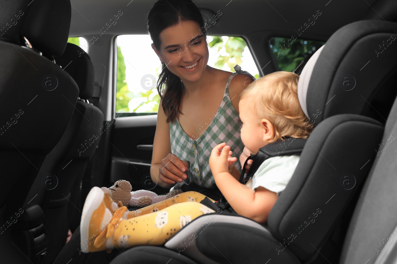 Photo of Mother fastening her daughter in child safety seat inside car