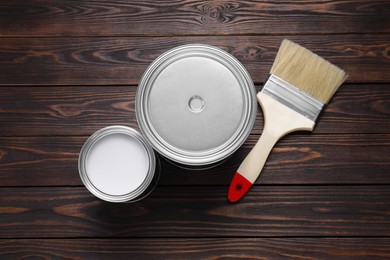 Can of white paint, closed one and brush on wooden table, flat lay