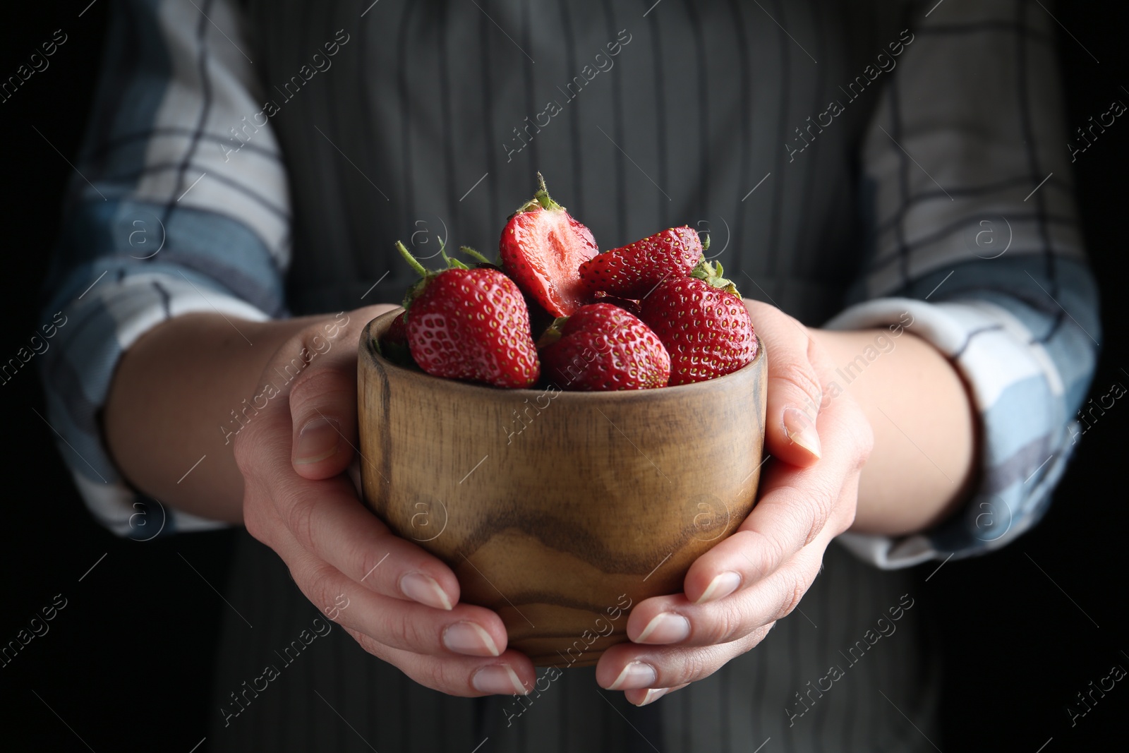 Photo of Woman holding bowl with tasty fresh strawberries on black background, closeup