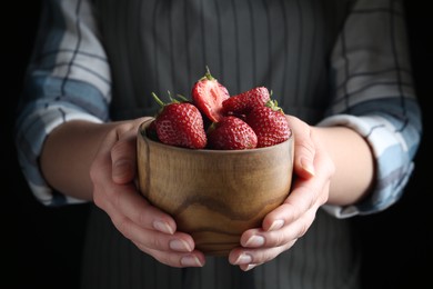 Photo of Woman holding bowl with tasty fresh strawberries on black background, closeup