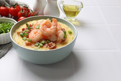 Photo of Fresh tasty shrimps, bacon, grits and green onion in bowl on white tiled table, closeup. Space for text
