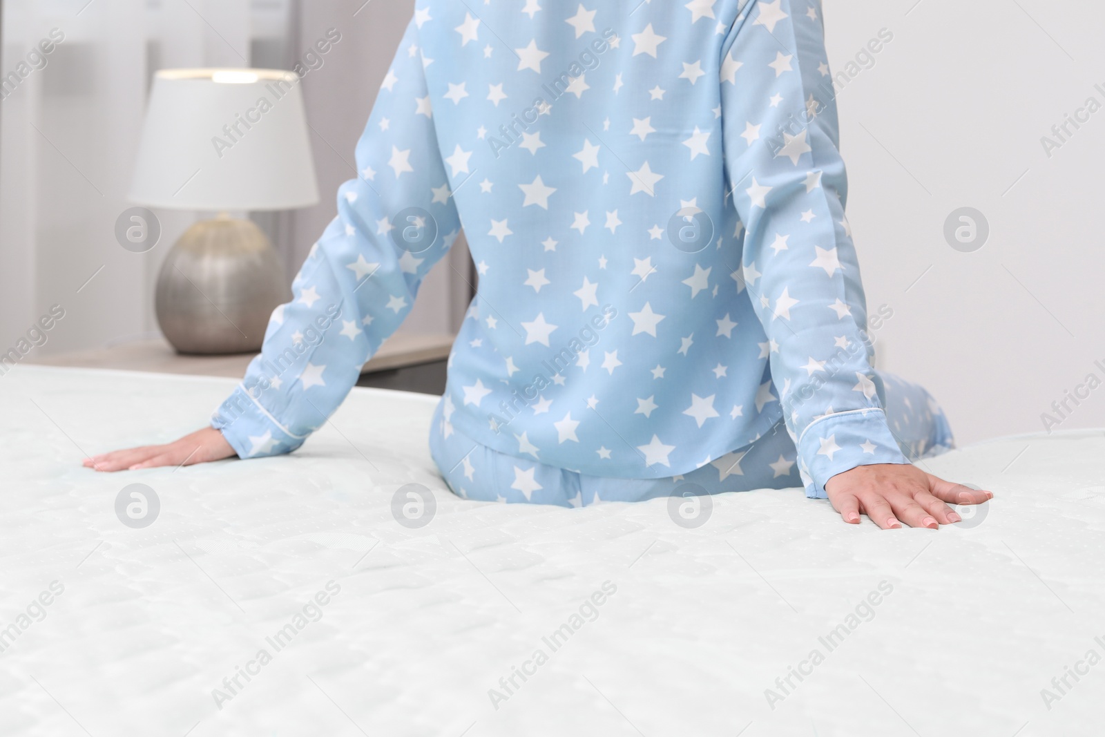 Photo of Woman sitting on new soft mattress in bedroom, closeup