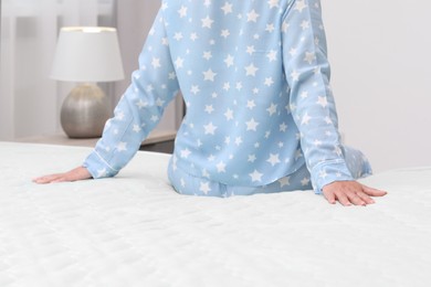 Photo of Woman sitting on new soft mattress in bedroom, closeup