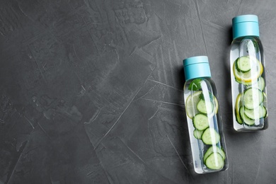 Photo of Bottles of refreshing water with cucumber, lemon and mint on black table, flat lay. Space for text