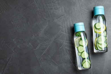 Bottles of refreshing water with cucumber, lemon and mint on black table, flat lay. Space for text