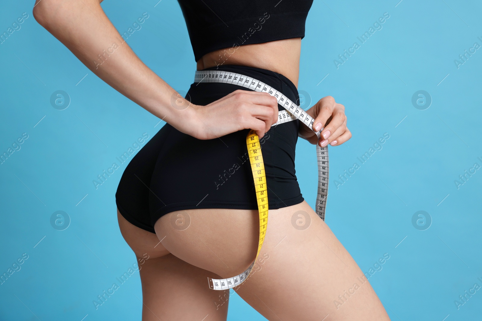 Photo of Young woman measuring waist with tape on light blue background, closeup