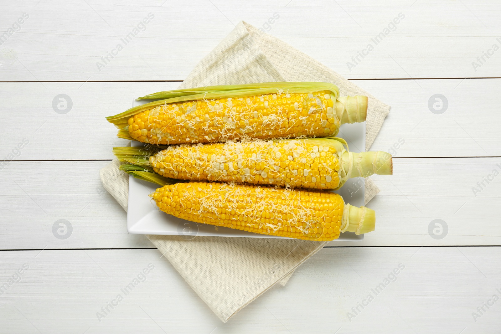 Photo of Plate with tasty cooked corn cobs on white wooden table, top view