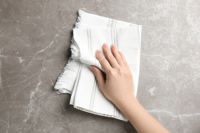 Photo of Woman wiping grey marble table with kitchen towel, top view