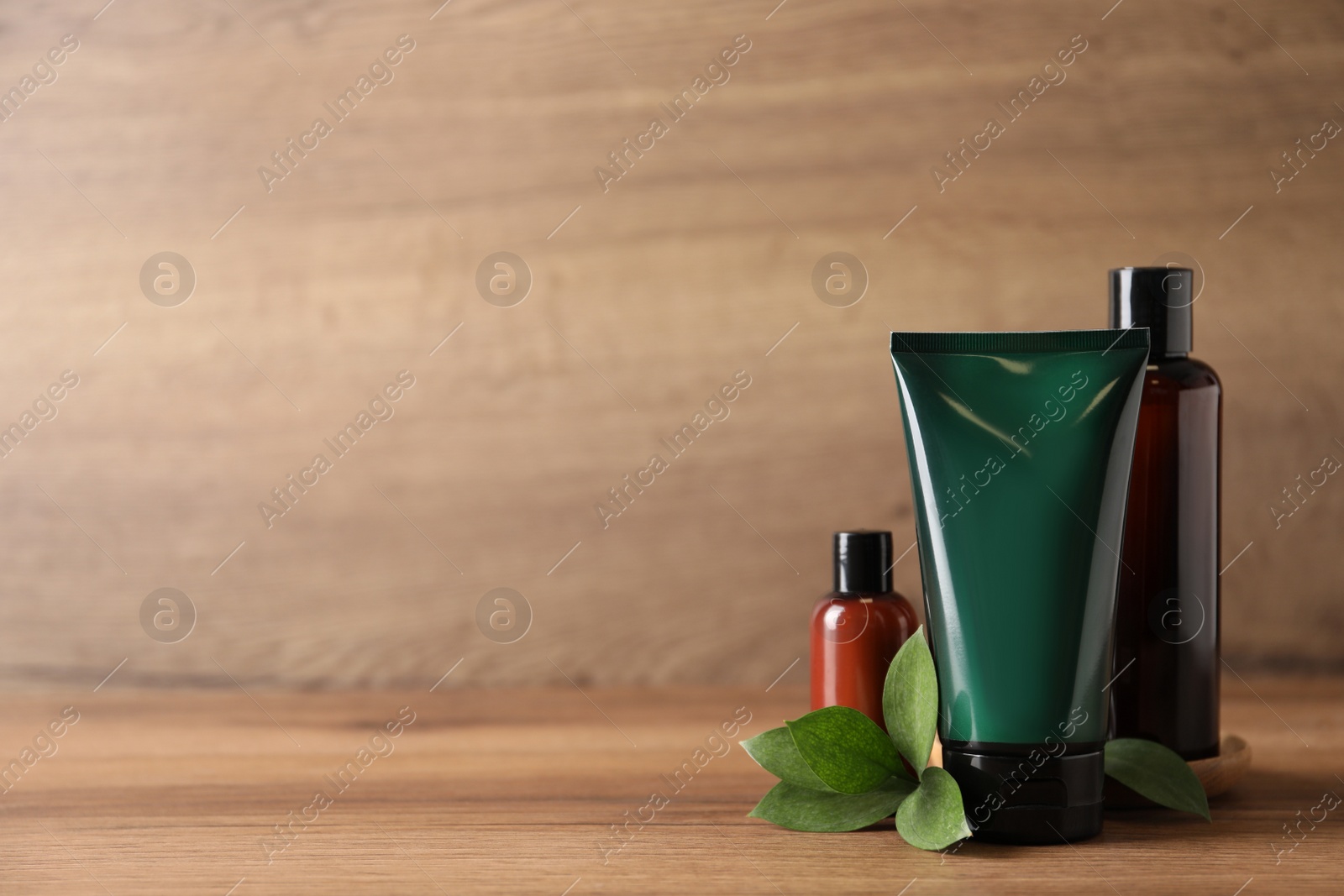 Photo of Facial cream and other men's cosmetic with green leaves on wooden table. Mockup for design