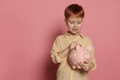 Photo of Cute little boy putting coin into piggy bank on pale pink background, space for text