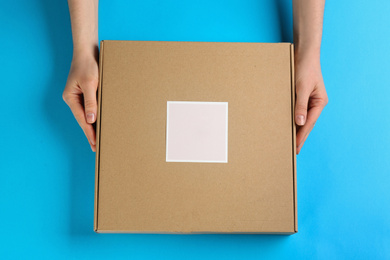 Woman holding cardboard box on light blue background, top view