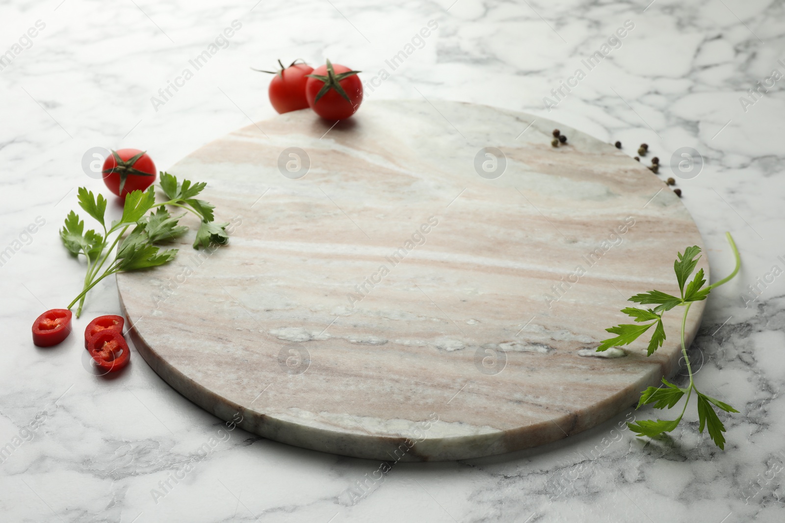 Photo of Cutting board, parsley, pepper and tomatoes on white marble table. Space for text