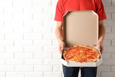 Photo of Young man with opened pizza box near white  brick wall, space for text. Food delivery service.