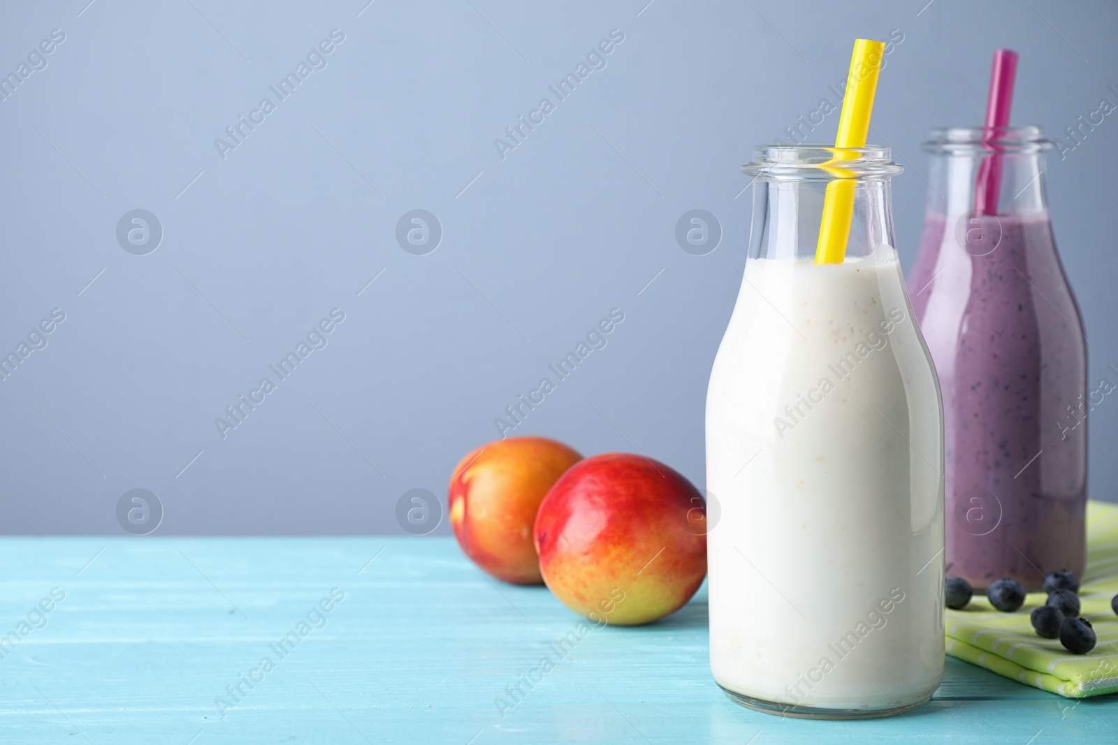 Photo of Tasty peach and blueberry milk shakes in bottles on light blue wooden table. Space for text