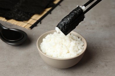 Photo of Holding nori with rice over grey table, closeup