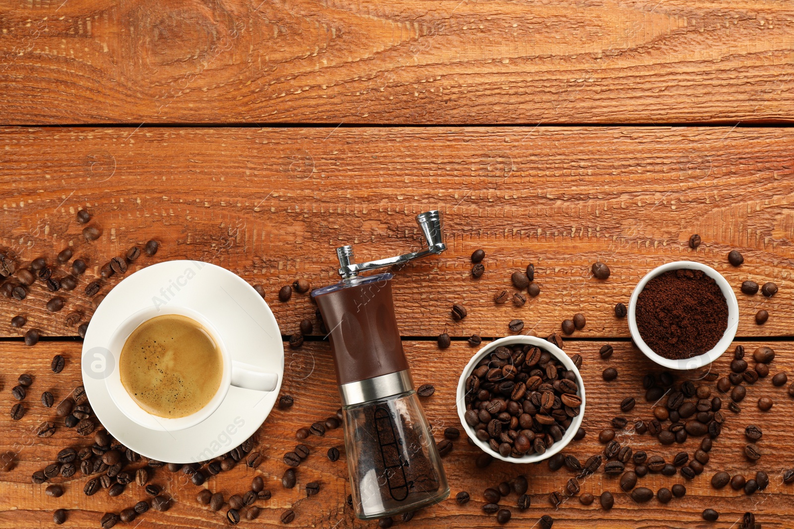 Photo of Modern manual coffee grinder with beans, powder and cup of aromatic drink on wooden table, flat lay. Space for text