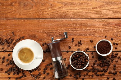 Modern manual coffee grinder with beans, powder and cup of aromatic drink on wooden table, flat lay. Space for text