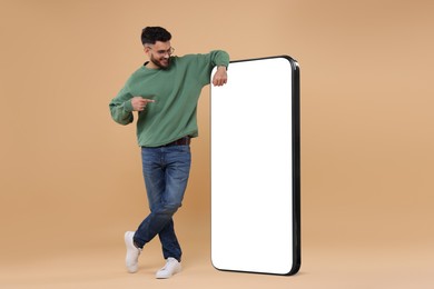 Man pointing at huge mobile phone with empty screen on dark beige background. Mockup for design