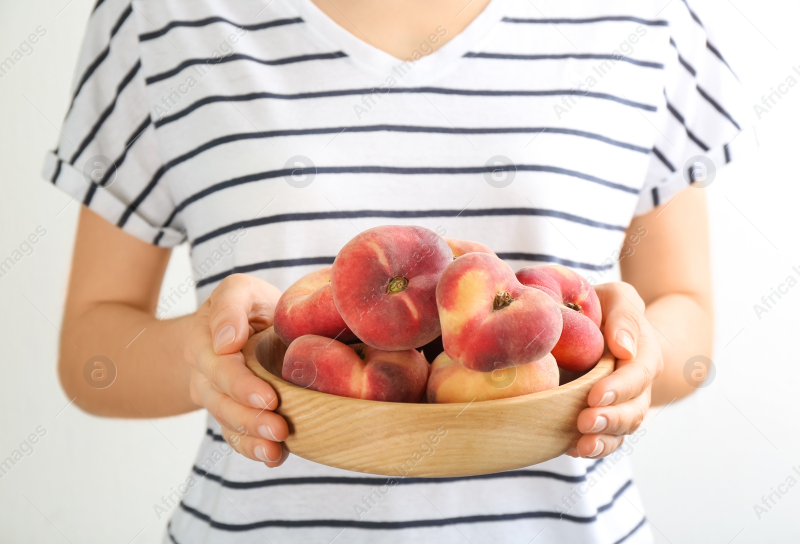 Photo of Woman holding bowl of fresh ripe donut peaches on light background, closeup