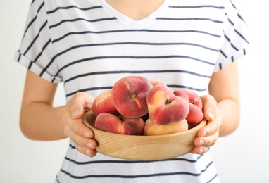 Photo of Woman holding bowl of fresh ripe donut peaches on light background, closeup