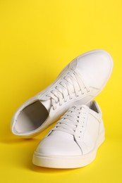 Pair of stylish white sneakers on yellow background