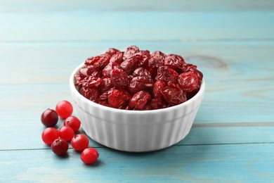 Photo of Tasty dried cranberries in bowl and fresh ones on light blue wooden table, closeup