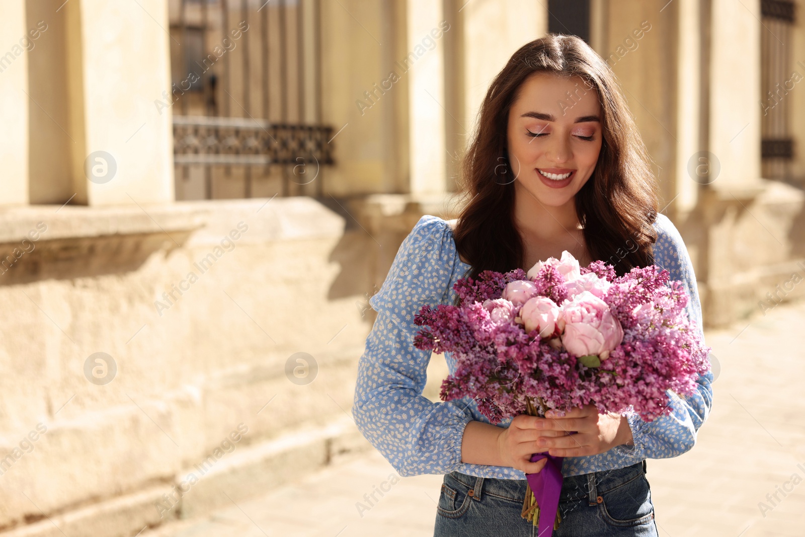 Photo of Beautiful woman with bouquet of spring flowers on city street, space for text