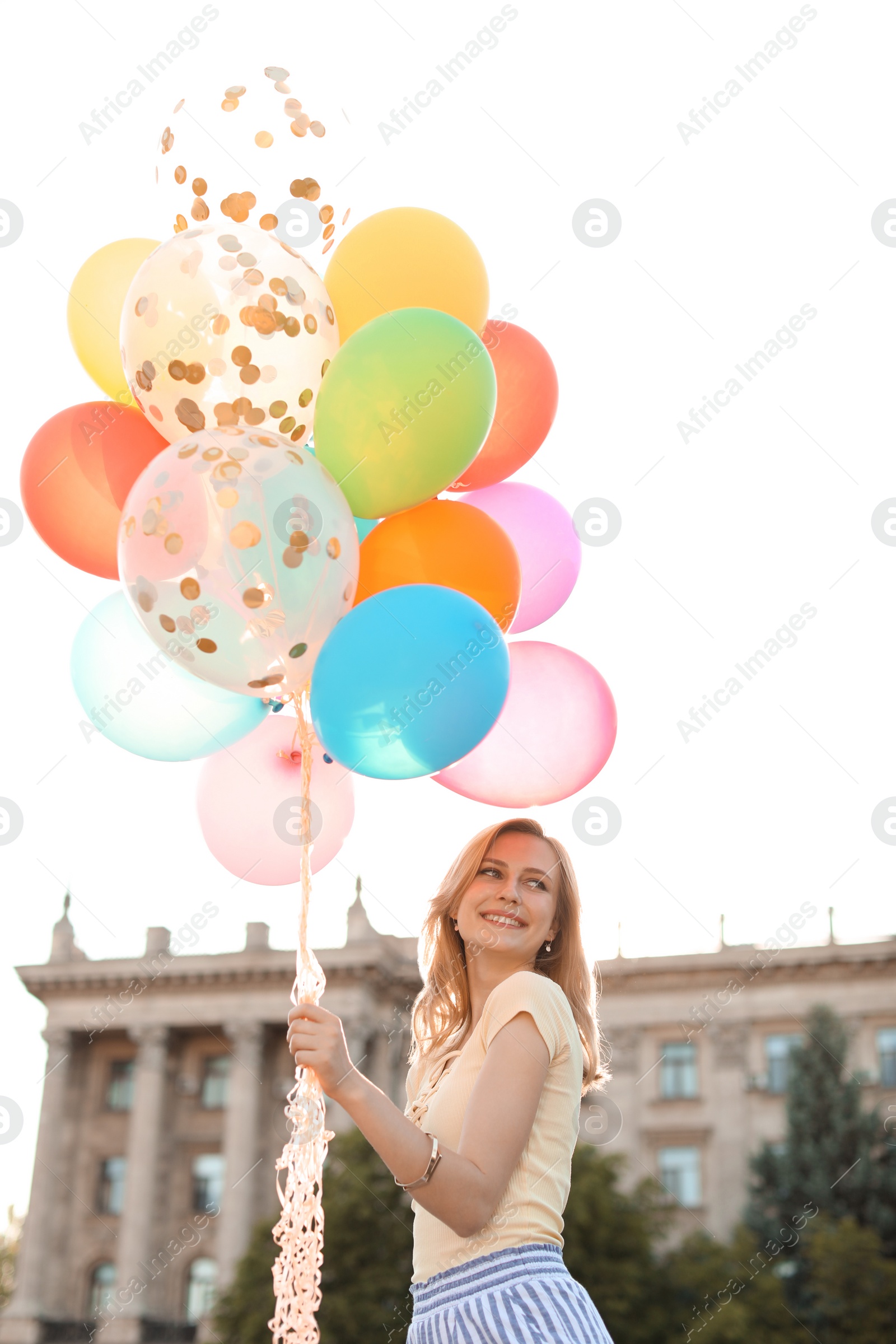 Photo of Young woman with colorful balloons outdoors on sunny day