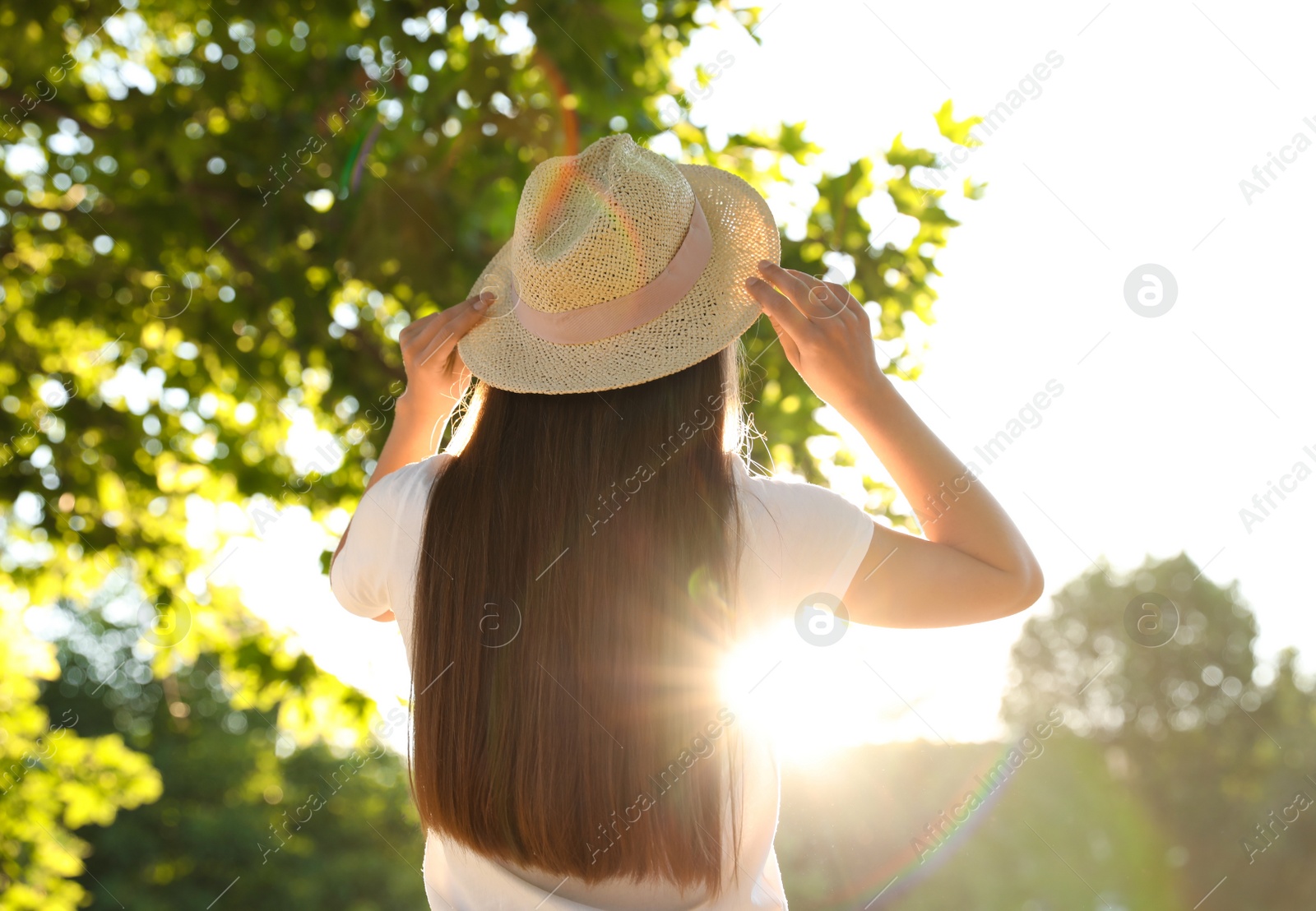 Photo of Young woman in hat outdoors on sunny day, back view