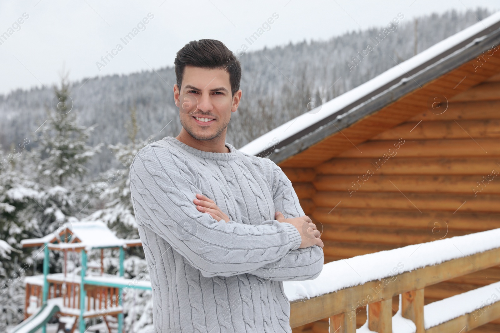 Photo of Happy man in warm sweater near wooden railing outdoors