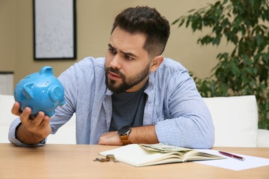 Young man with piggy bank at table indoors. Money savings