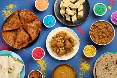 Traditional Indian food and color powders on blue background, flat lay. Holi festival celebration