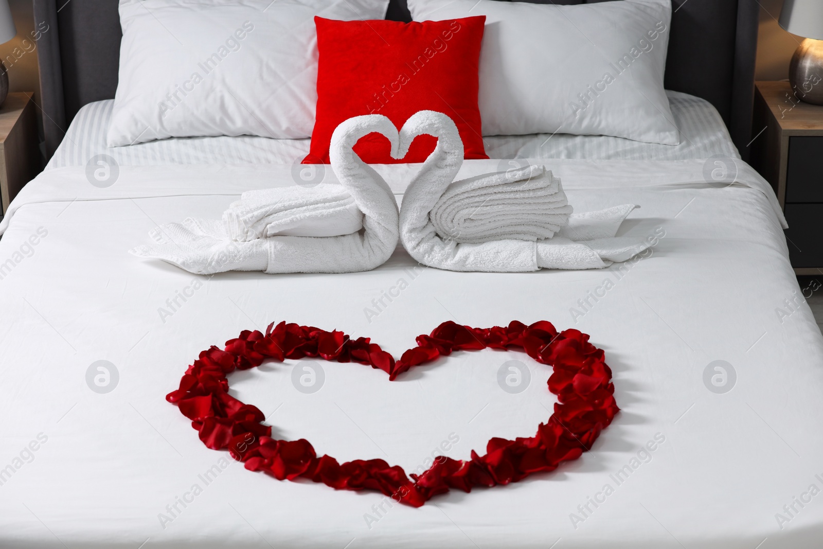 Photo of Honeymoon. Swans made with towels and heart of beautiful rose petals on bed in room