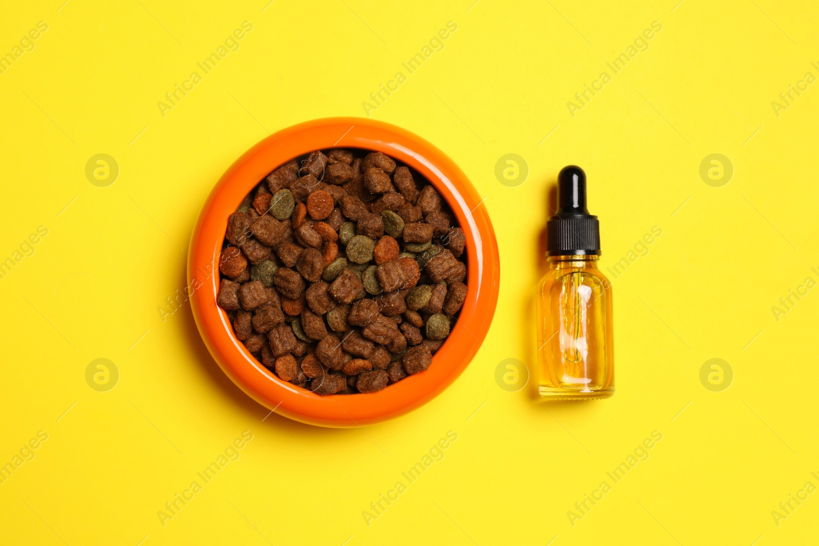 Photo of Glass bottle of tincture near bowl with dry pet food on yellow background, flat lay