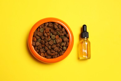 Photo of Glass bottle of tincture near bowl with dry pet food on yellow background, flat lay