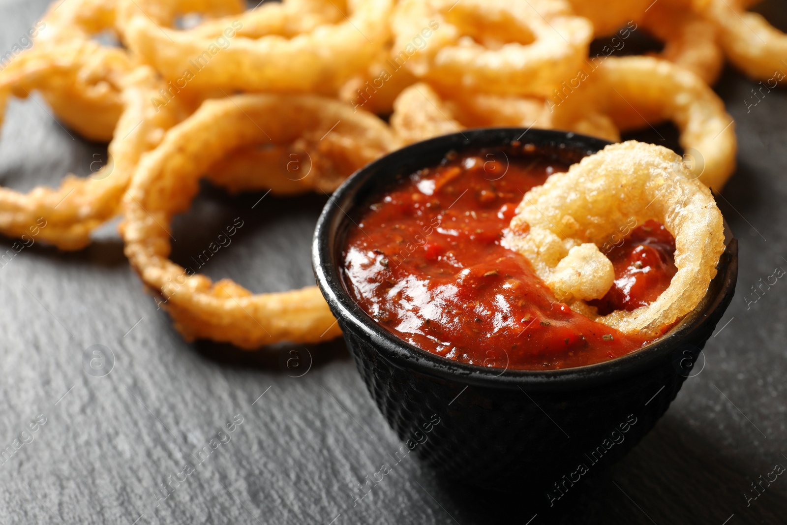 Photo of Homemade crunchy fried onion rings with tomato sauce on table, closeup