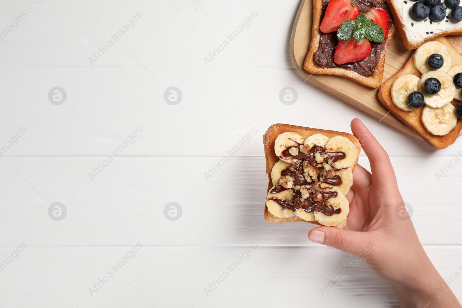 Photo of Woman holding delicious sweet toast at white wooden table, top view. Space for text