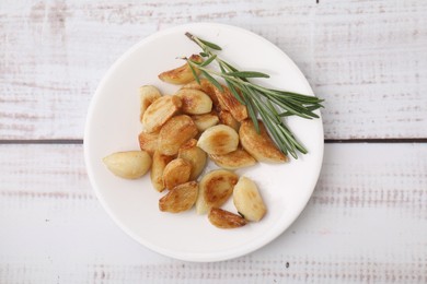 Photo of Fried garlic cloves and rosemary on wooden table, top view